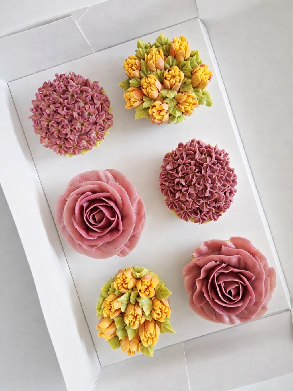 Blumen-Cupcakes in einer Box in Violett, Orange und Gelb